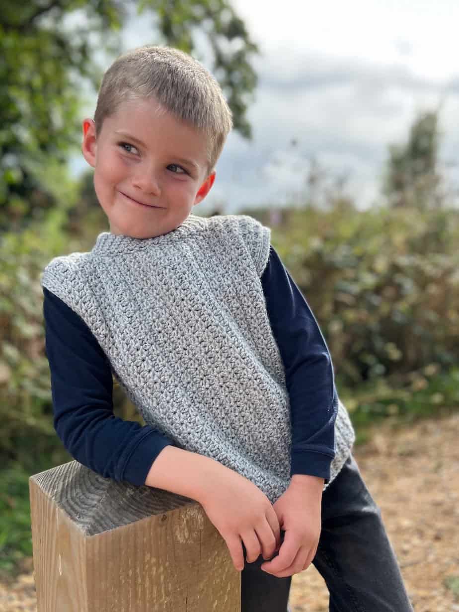 Boy smiling wearing baby crochet vest pattern in grey.