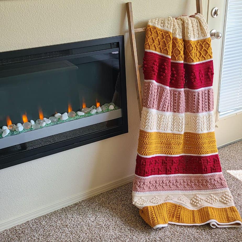 Textured crochet blanket hanging on a ladder next to a fireplace.
