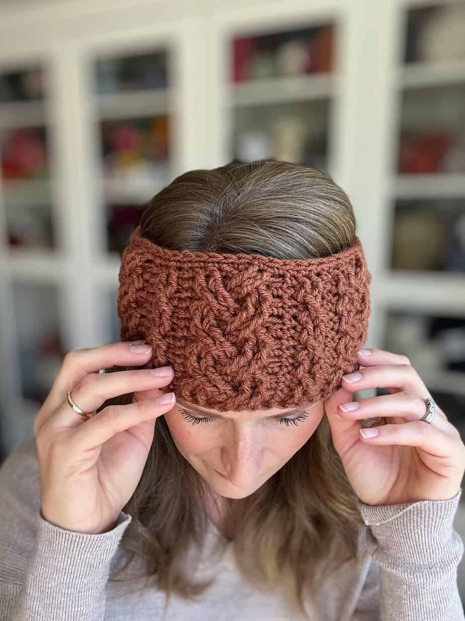 Woman looking down putting on crochet headband with cable stitches on it.