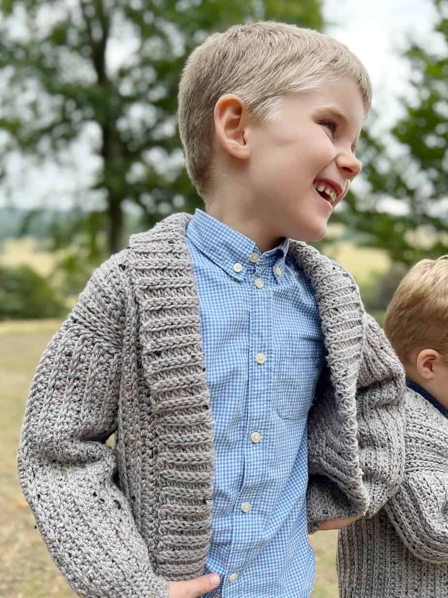 Five year old boy smiling wearing a crochet cardigan.