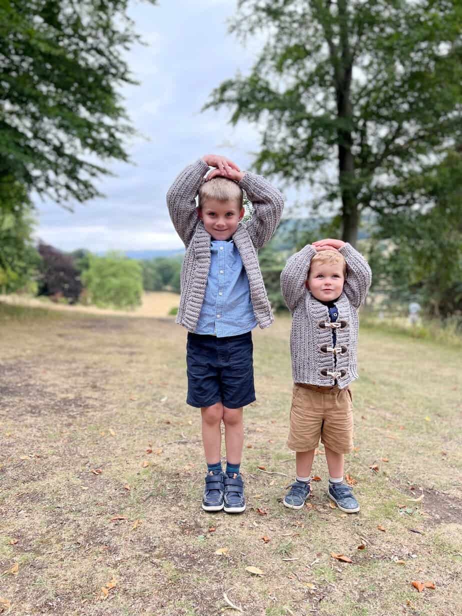 Two boys with hands on heads wearing cardigans and shorts.