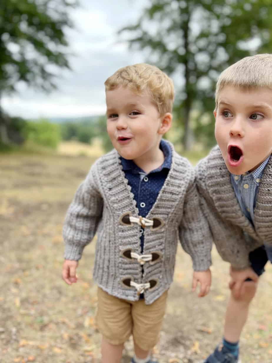 Two boys in child crochet cardigan pattern with toggles and long sleeves.