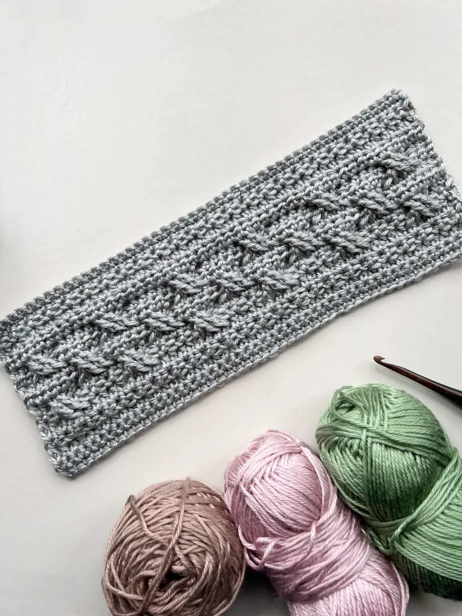 Crochet cable stitch pattern in grey yarn with wooden crochet hook.