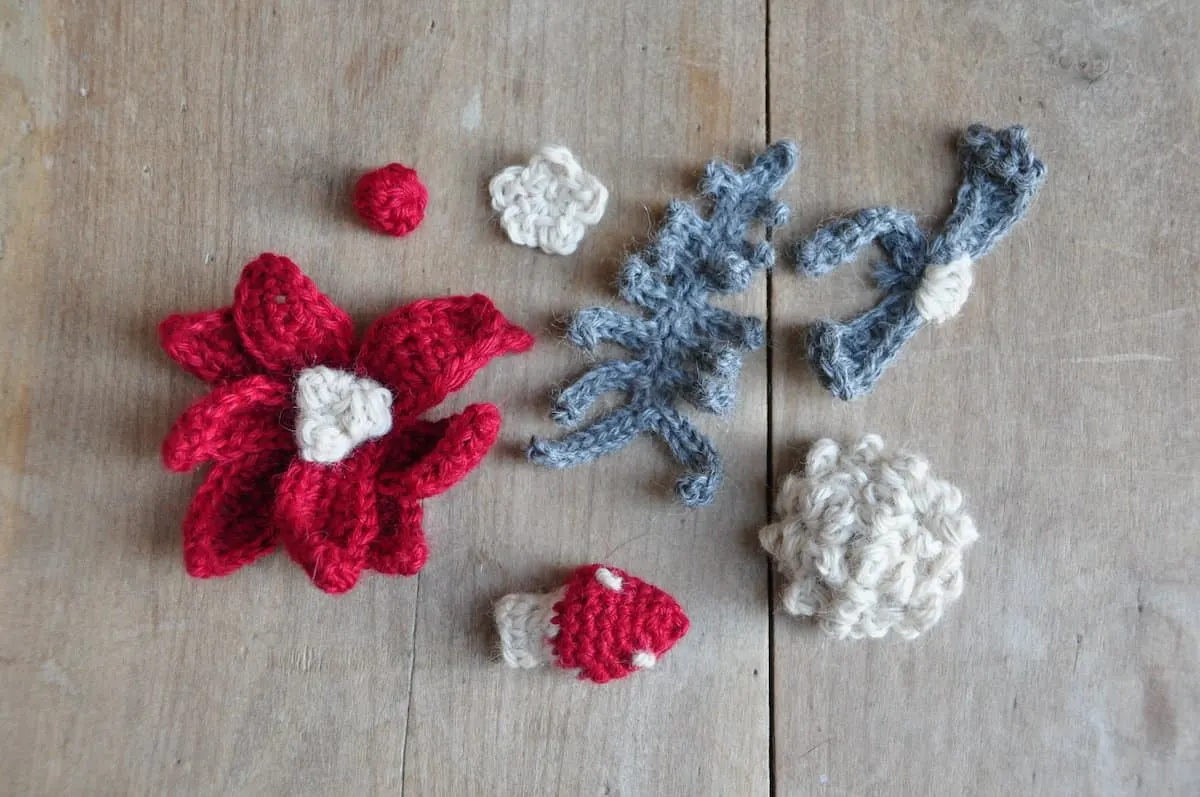 Selection of crochet mistletoe, poinsettia, toadstool, fern and pine cone laying on a table.