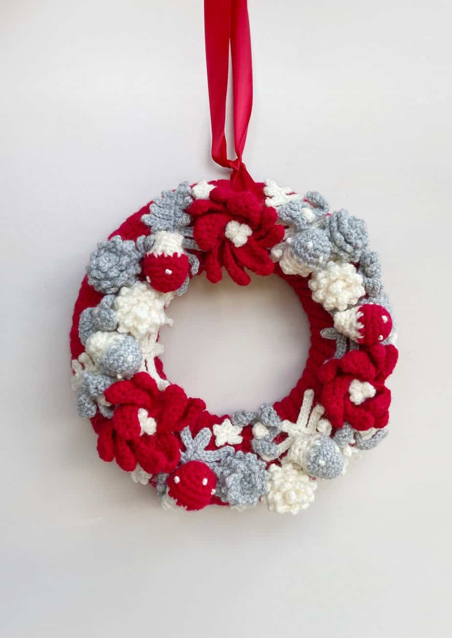 Christmas crochet wreath with poinsettias, mistletoe and a red ribbon hanging on a wall.