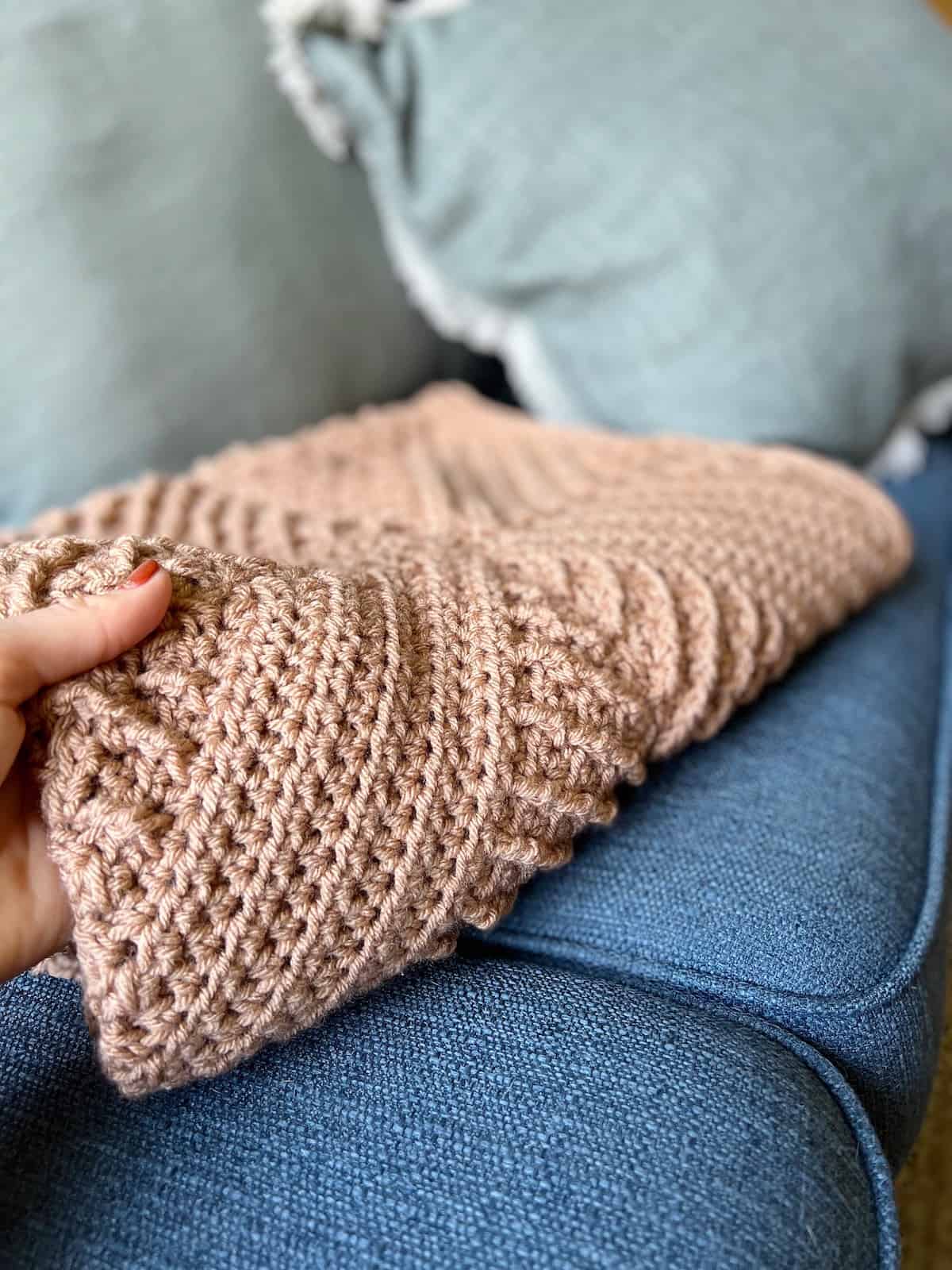 Hand holding side of folded textured crochet blanket.