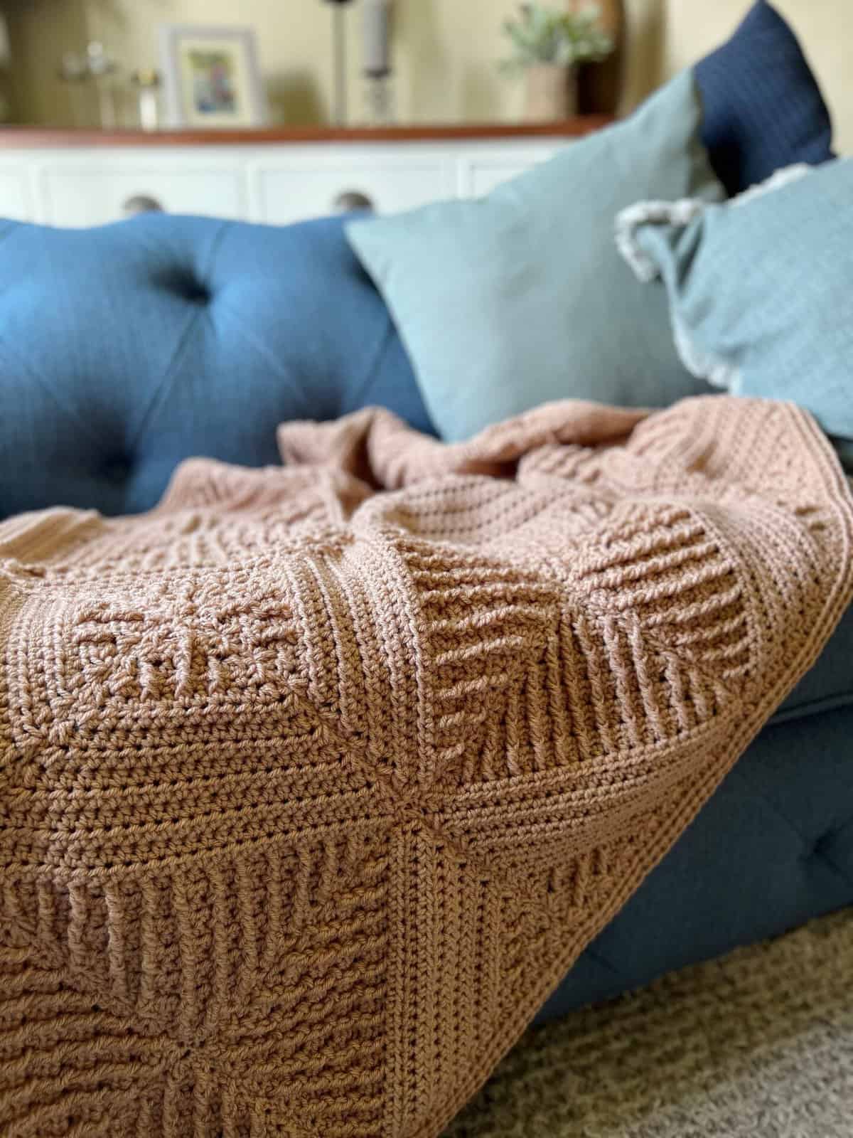 Crochet blanket using textured stitches laid on a sofa.