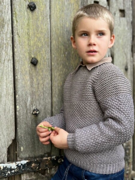 Crochet sweater pattern for boys on a 5 year old leaning against a door.