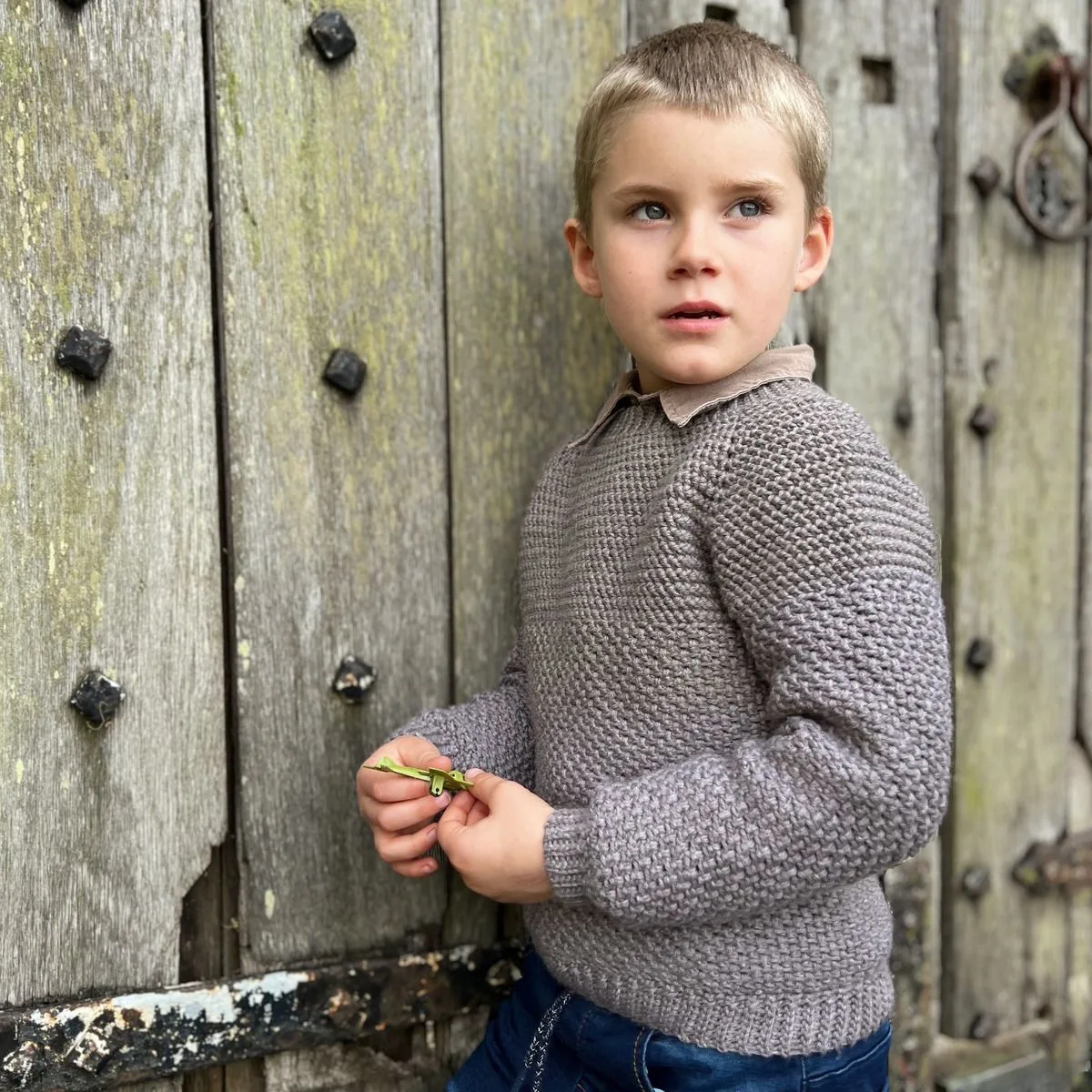 Crochet sweater pattern for boys on a 5 year old leaning against a door.