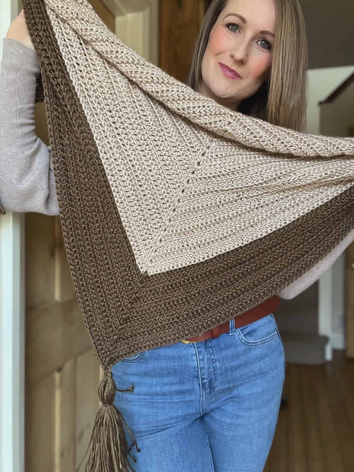 Woman holding up easy crochet shawl in cream and brown with tassels.