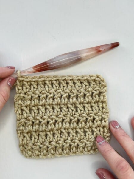 Image of stacked single crochet stitches in a crochet swatch with hook and hands.