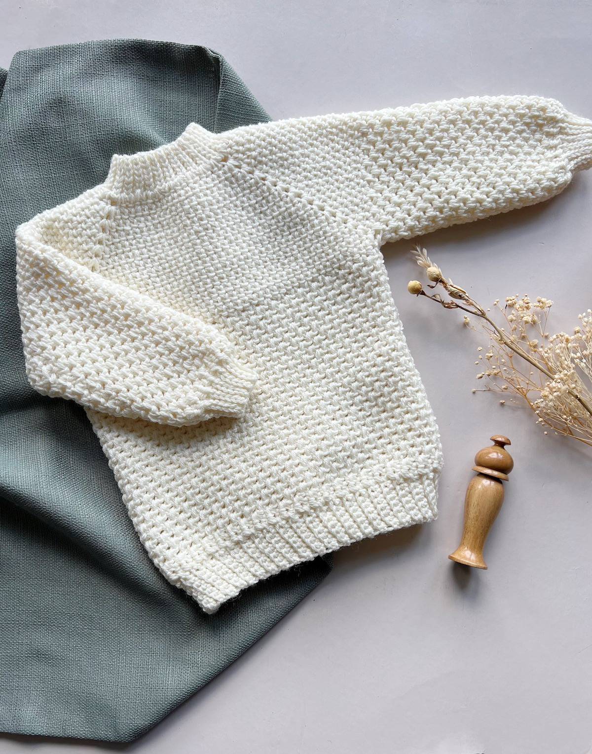 Seamless baby crochet sweater pattern with textured stitch in cream yarn.