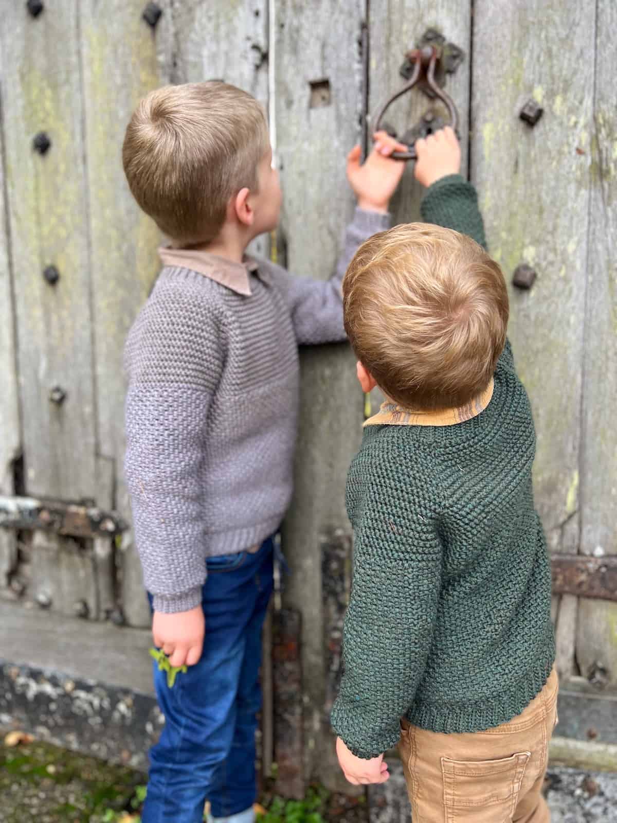 Two boys in seamless crochet sweaters holding onto old door handle.