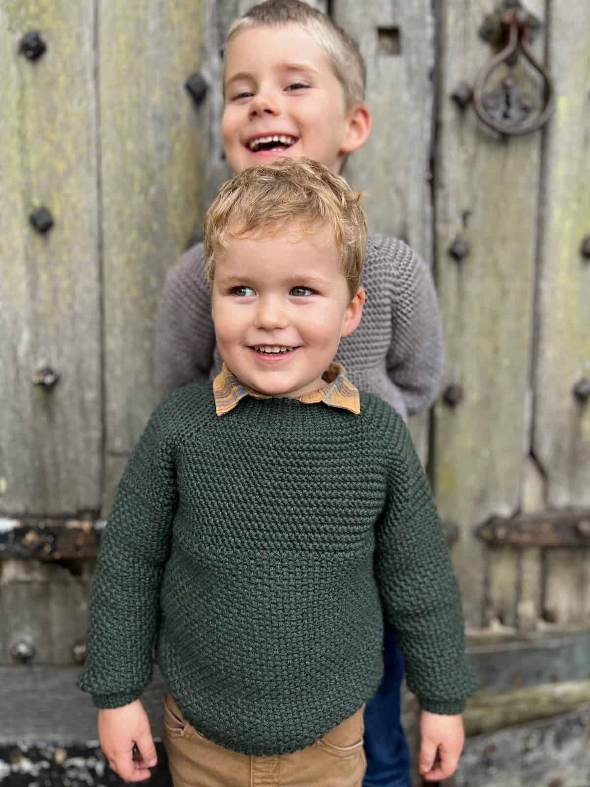 Boys in crochet sweaters standing behind each other smiling.