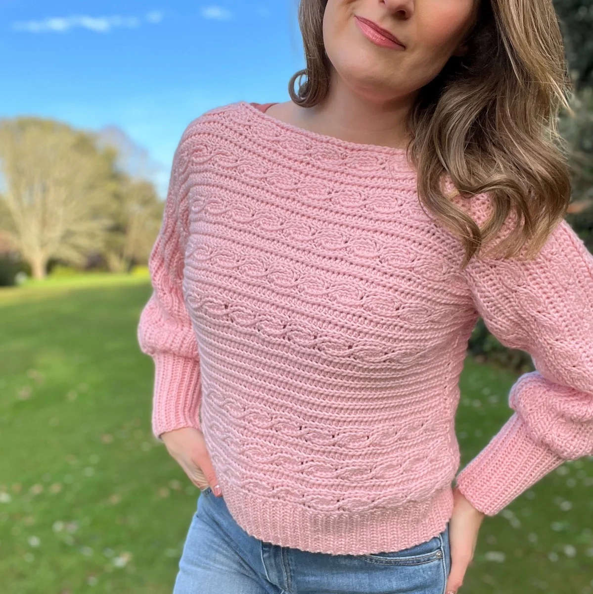 Woman wearing pink crop crochet sweater that has knit look crochet cables in short rows.
