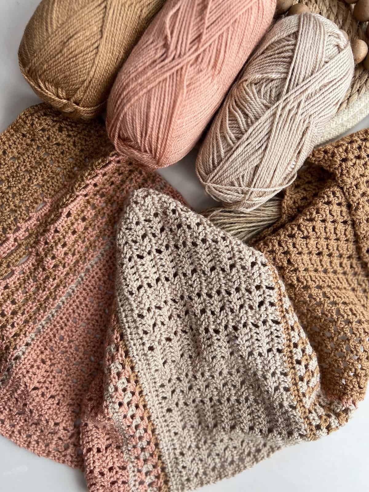 Feminine crochet scarf pattern laid on table with 3 balls of yarn.