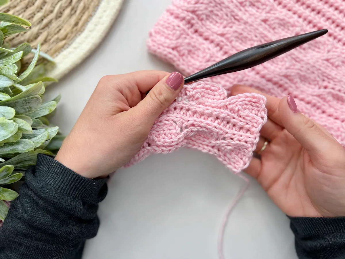Hands holding crochet hook and knit look crochet stitch sample in progress.