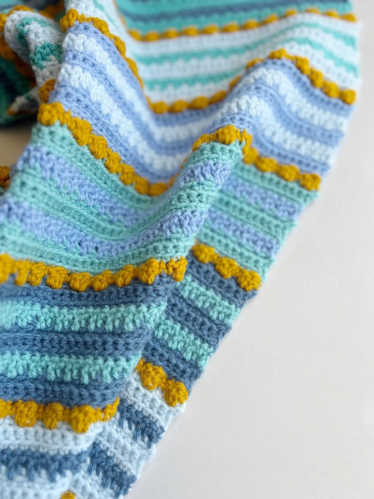 Close up of modern crochet baby blanket with mustard bobble stitches.