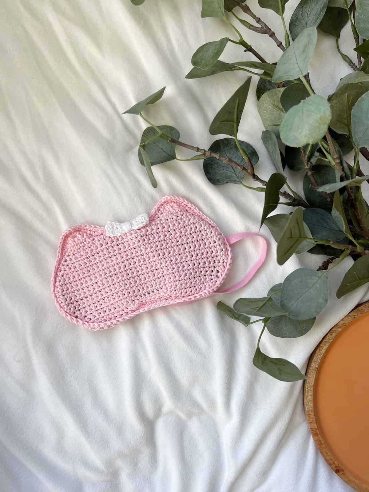 Pink crochet eye mask with cat ears and a bow.