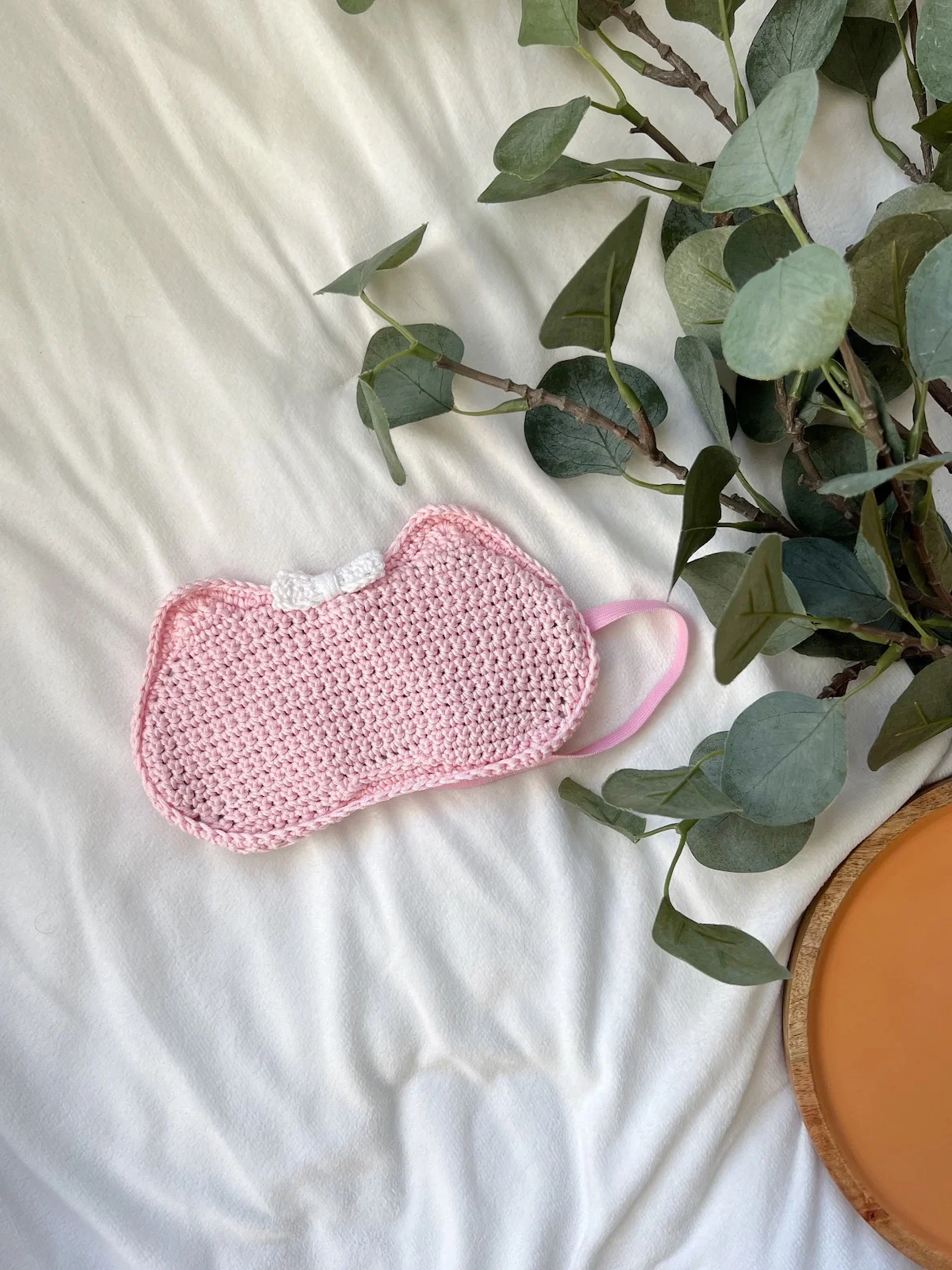 Pink crochet eye mask with cat ears and a bow.
