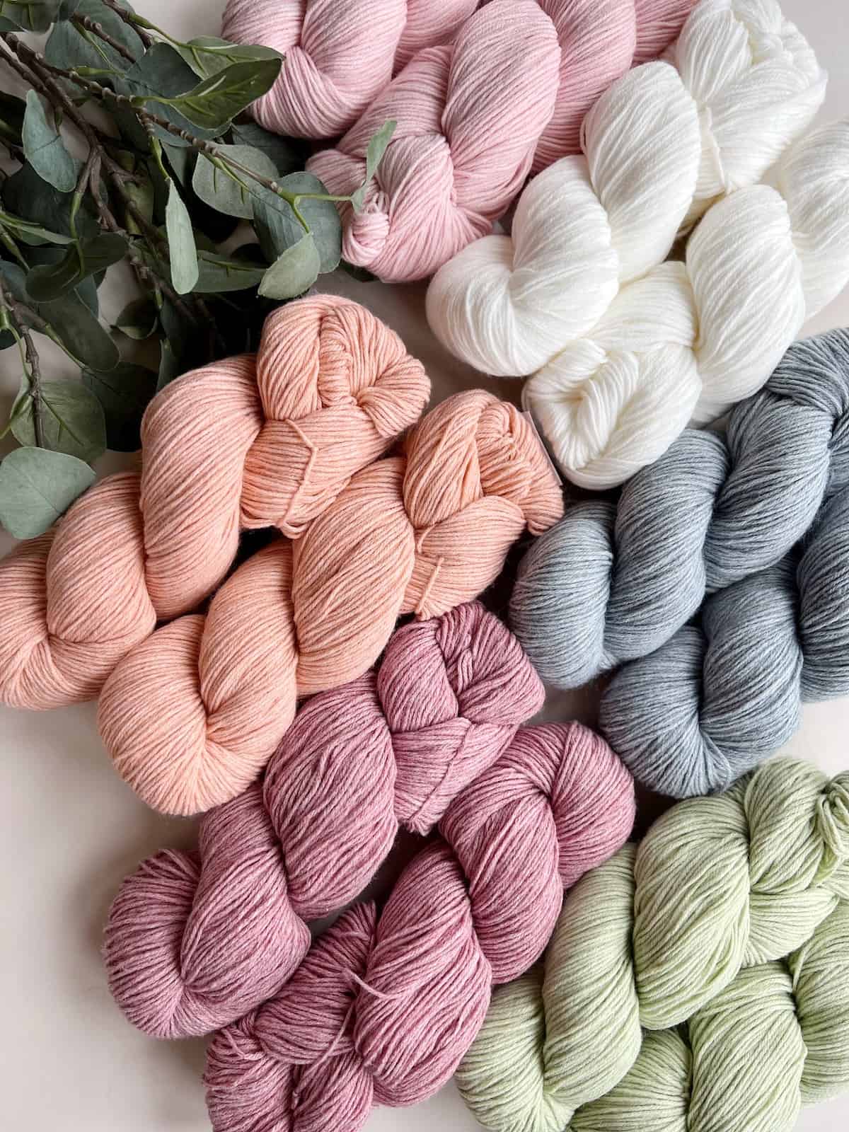 Hanks of pink, peach, blue, green and white yarn together on a table.
