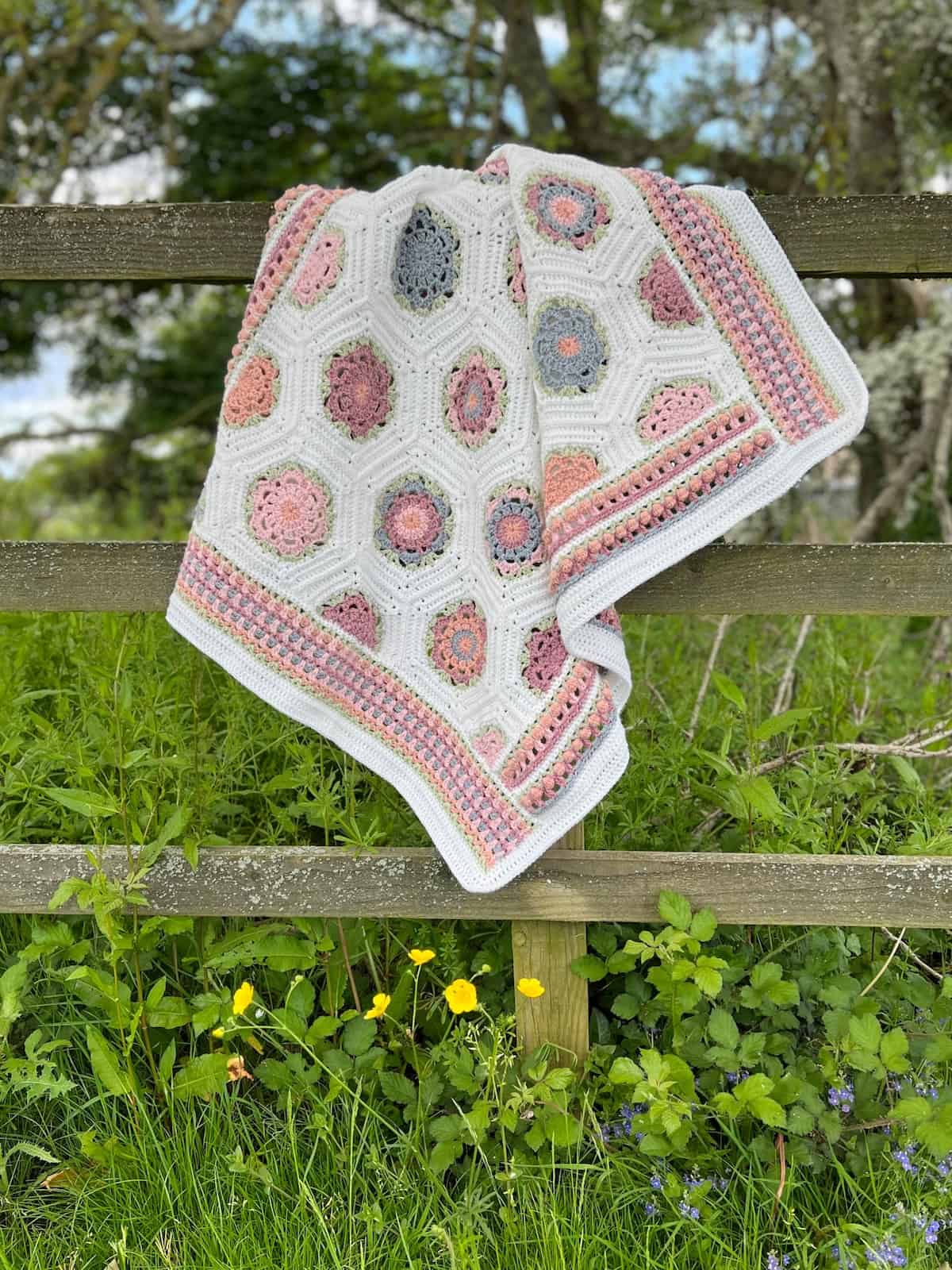 Crochet blanket made with hexagon motifs and flower stitches hanging on a gate.