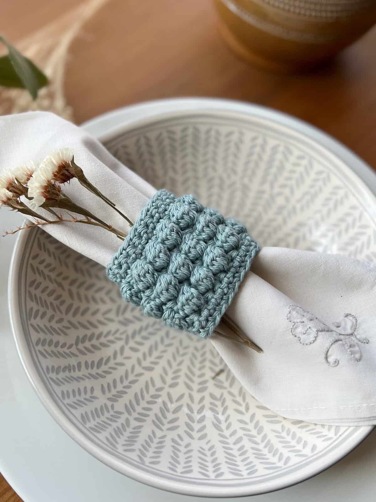 Crochet napkin ring with linen napkin and sprig of flowers.