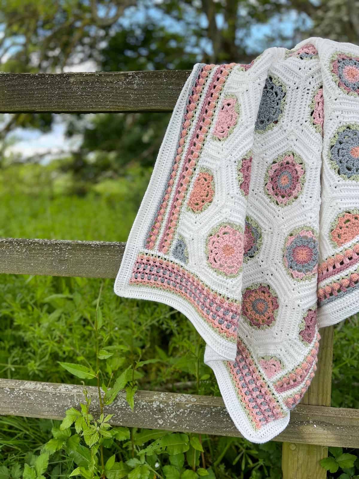 Floral crochet blanket draped over a gate in a field.