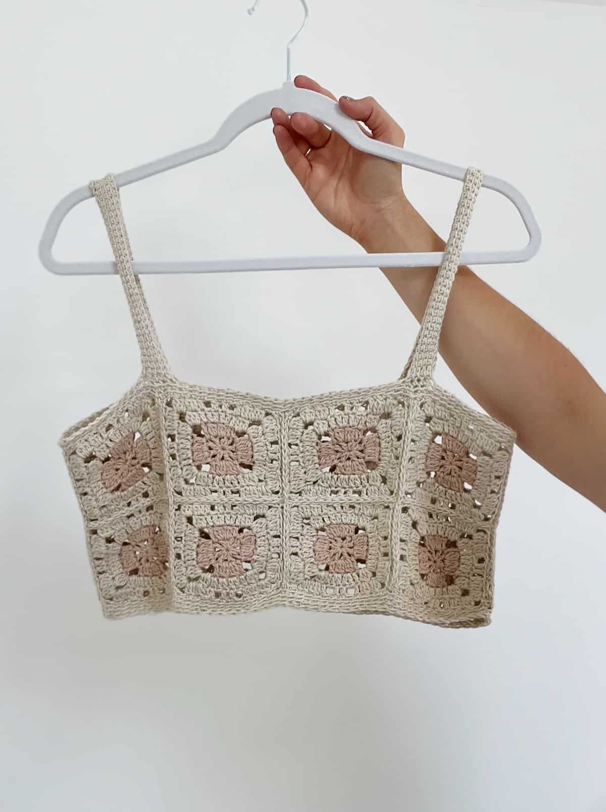Person holding up a crochet top made from squares on a hanger.