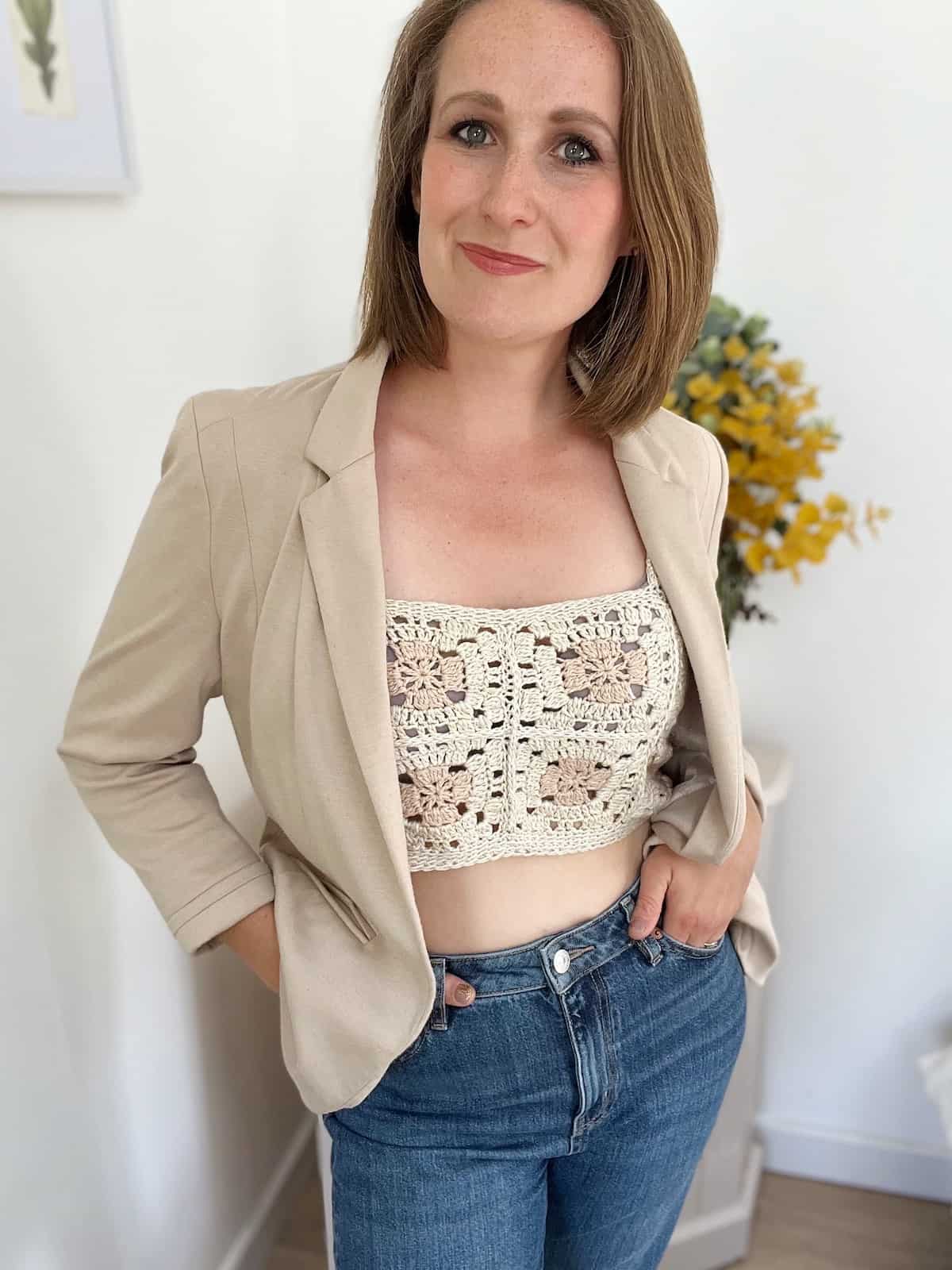 Woman wearing a crop crochet top under a cream jacket.