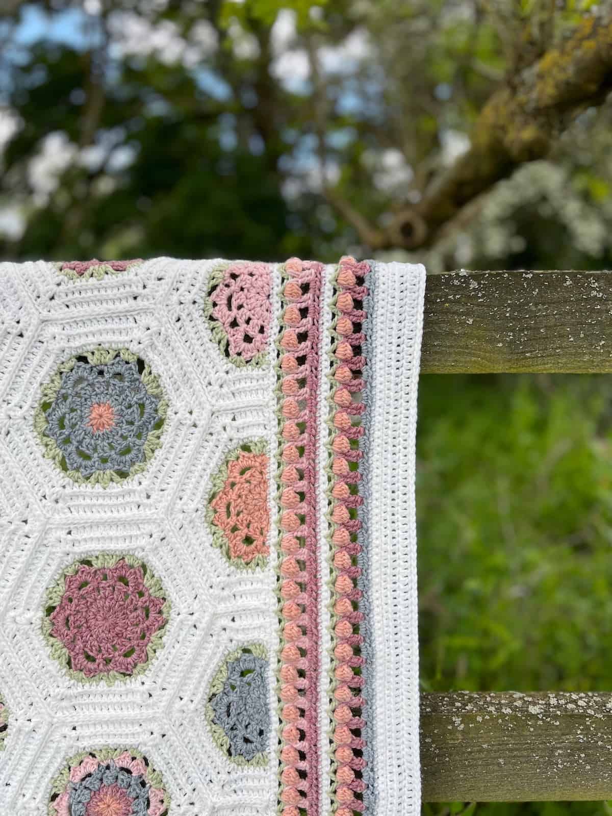 Blanket with hexagon crochet flower border on edge in pastel colours.