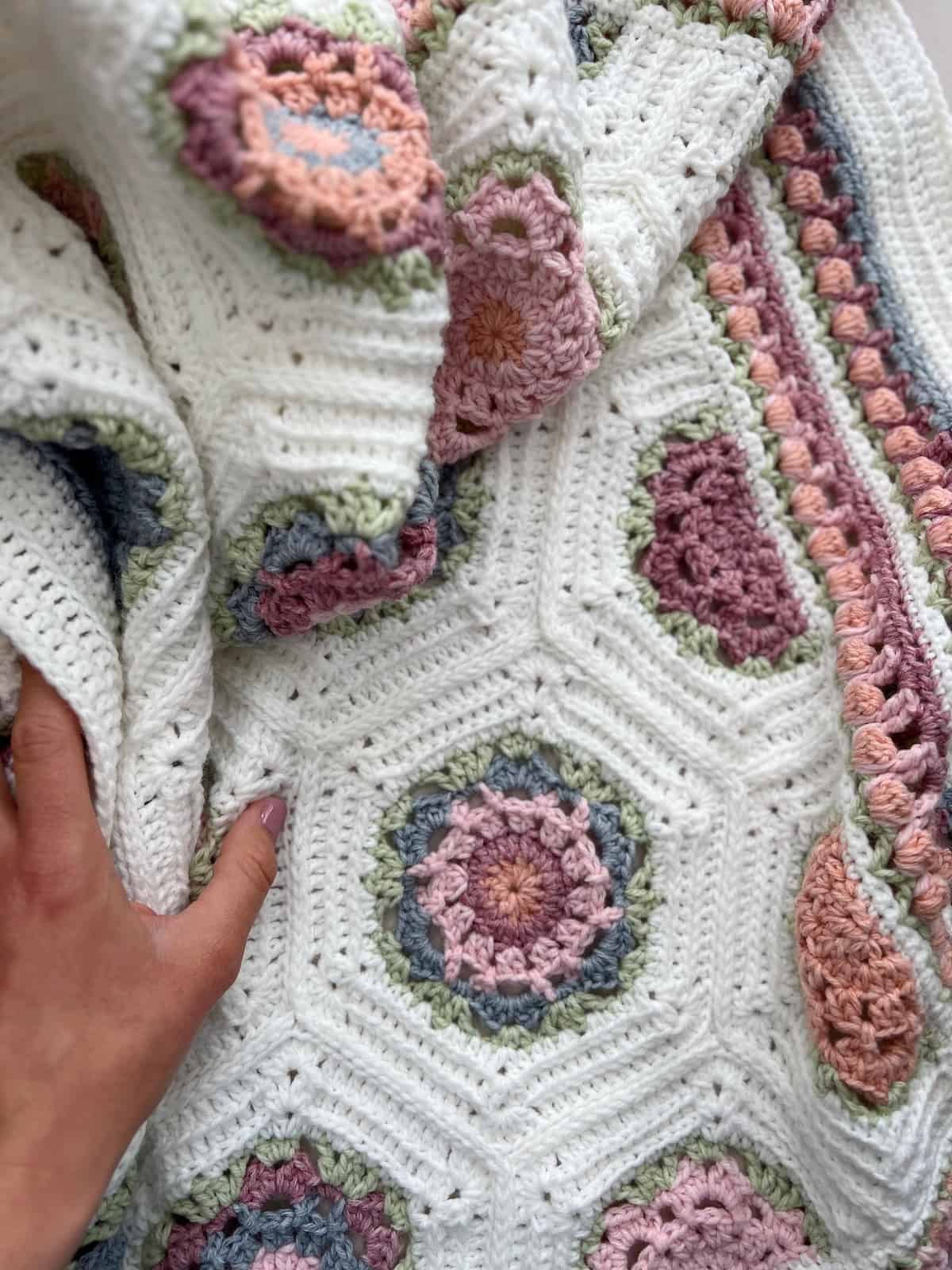 Persons hand scrunching up a crochet blanket made of hexagons and crochet half hexagons.