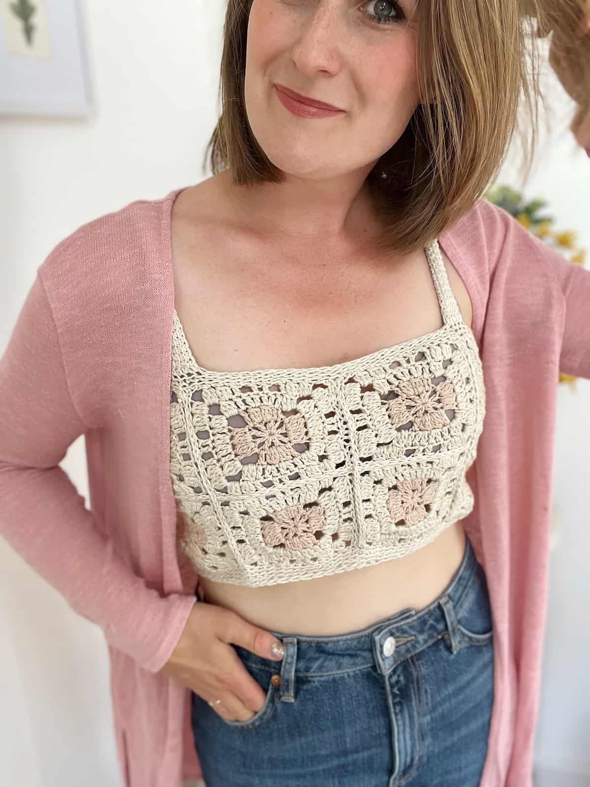 Woman wearing summer crochet crop top with straps underneath a pink long cardigan.