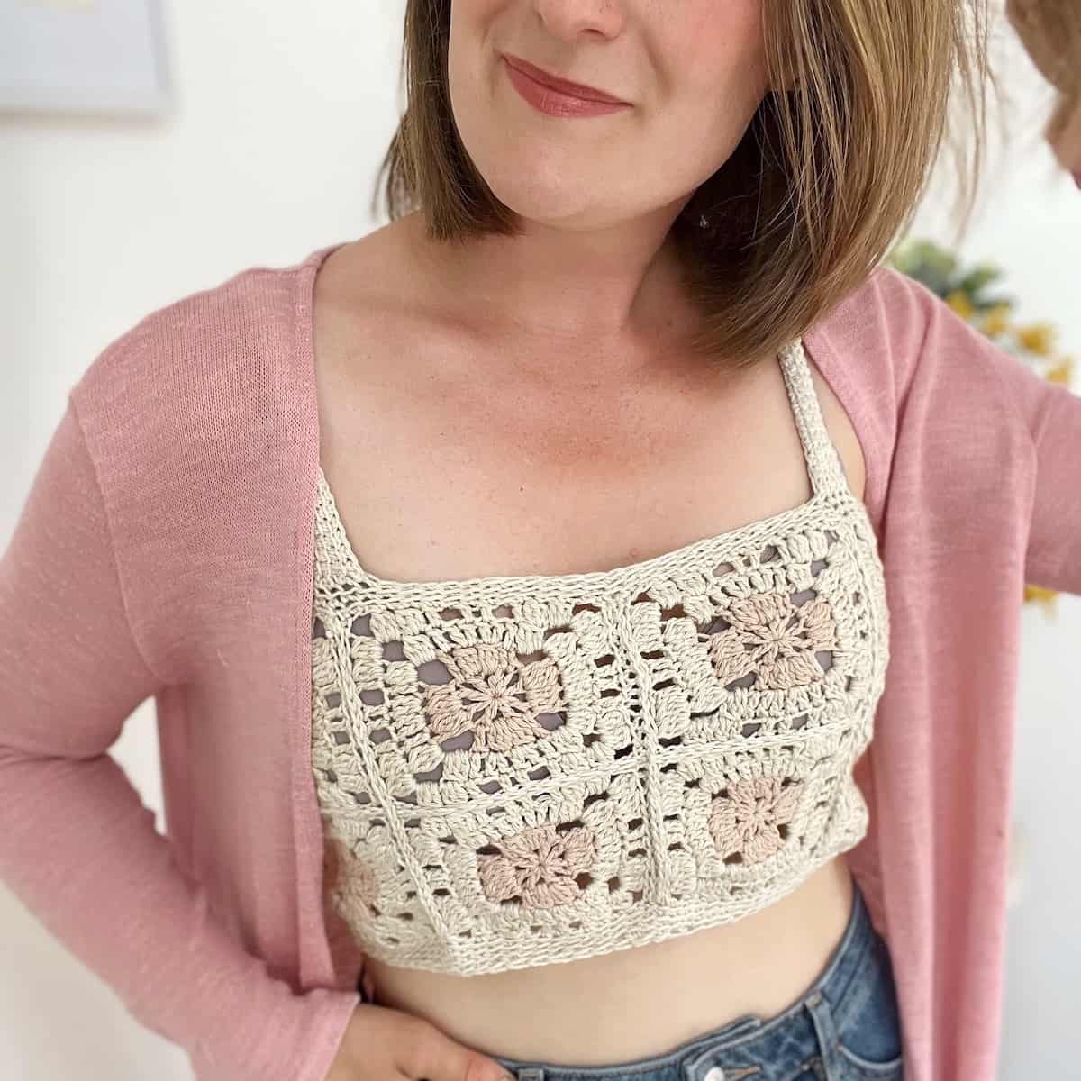 Woman wearing crochet crop top pattern with light pink cardigan over the top.