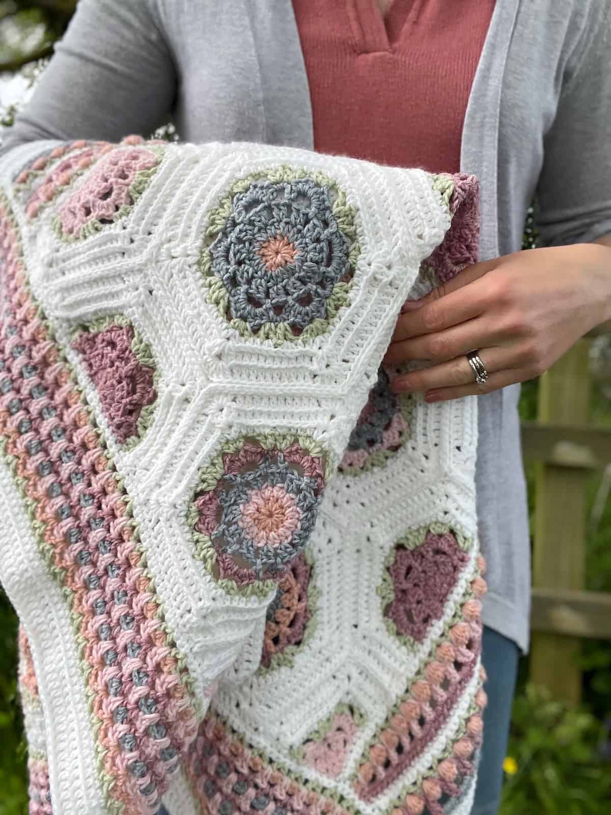 Pretty crochet blanket draped over someones arm in pastel colours.
