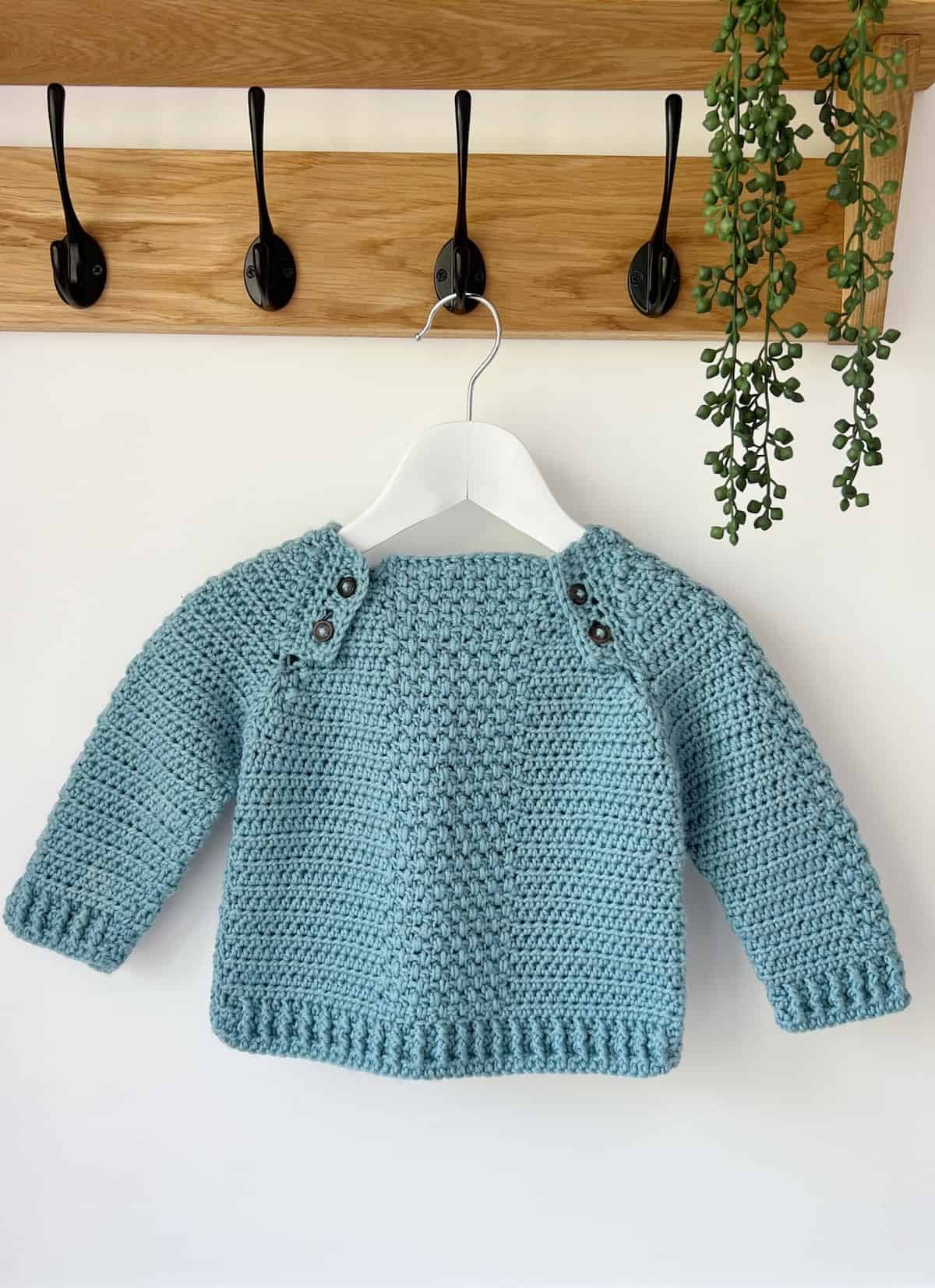 Baby crochet sweater in teal blue hanging up on a hook.