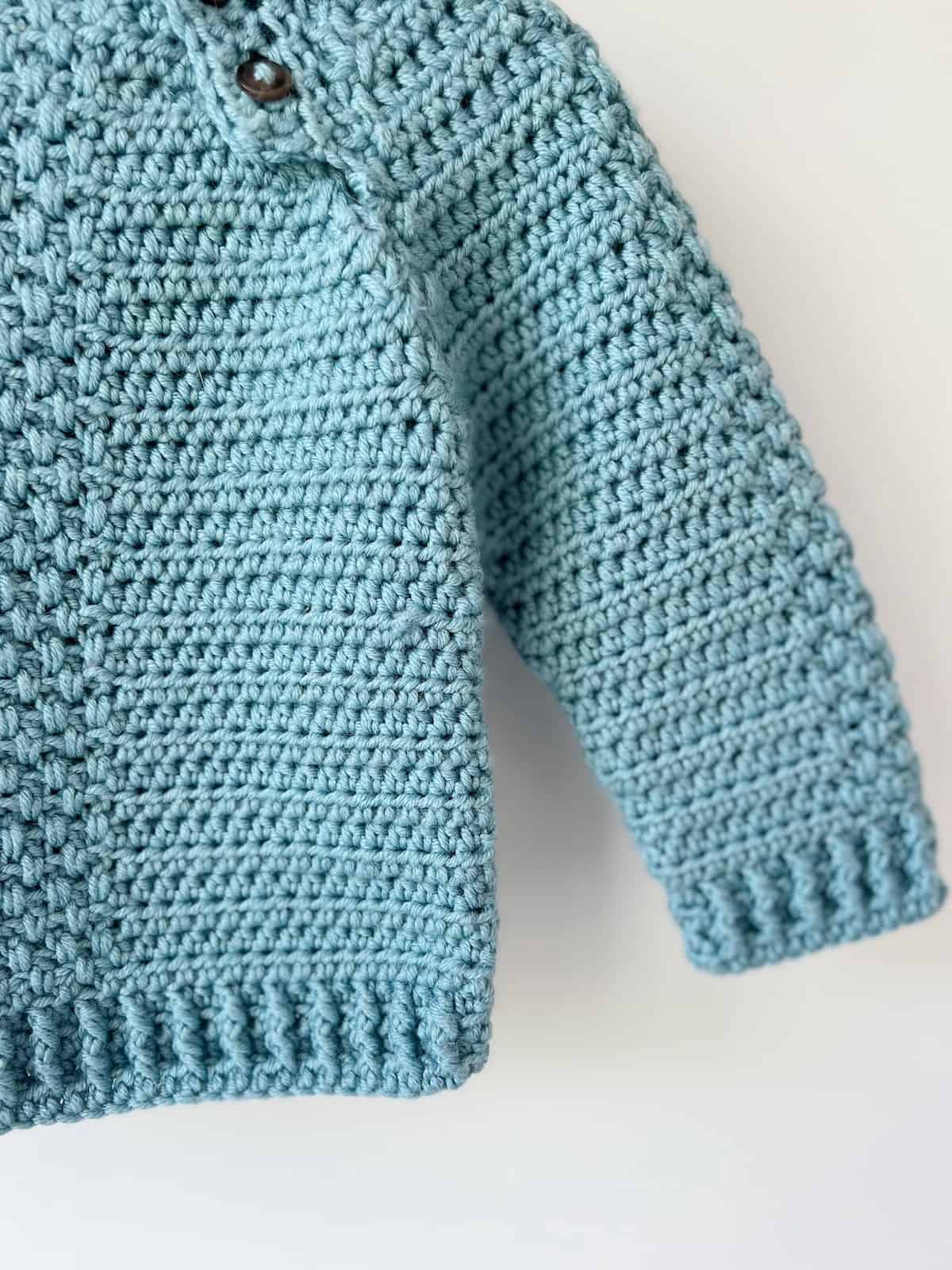 Close up of crochet sweater for babies with front and back post stitch cuffs.