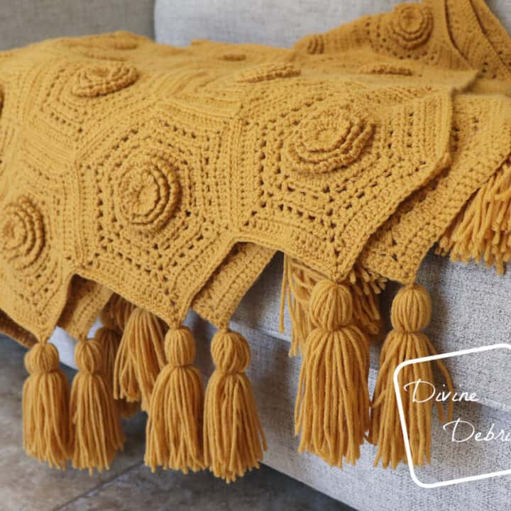A yellow crocheted blanket with tassels on a couch.