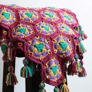 A colorful crocheted hexagon blanket with tassels on a stool.