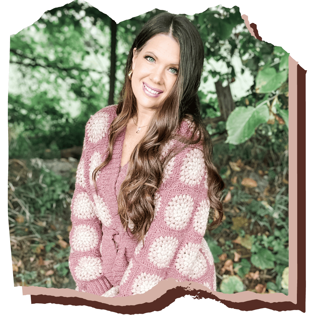 A woman in a pink cardigan is posing for a photo in the woods.