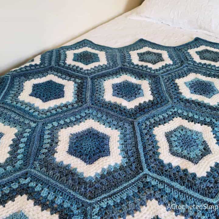 A blue and white crocheted afghan on a bed.