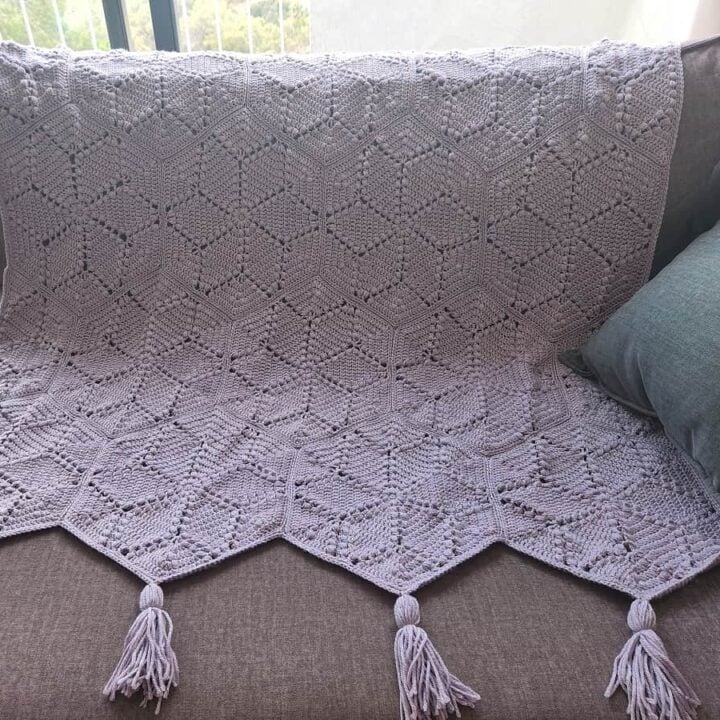 A crocheted blanket on a couch with tassels.