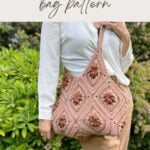 A person holds a large Granny Square Bag Crochet, featuring textured floral motifs, while standing outdoors near green bushes.