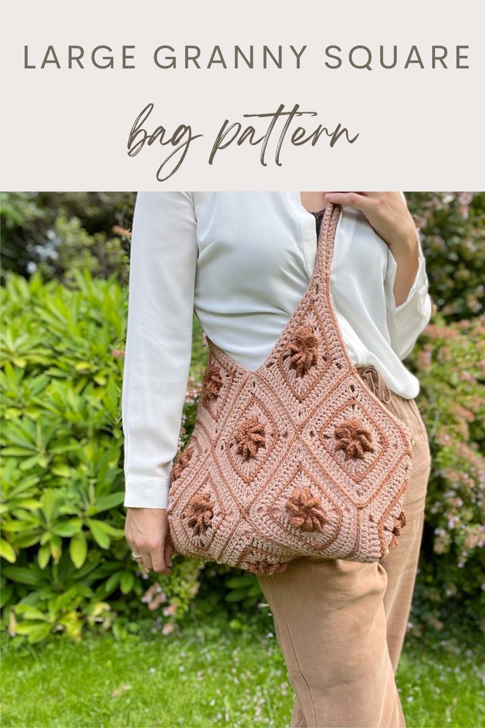A person holds a large Granny Square Bag Crochet, featuring textured floral motifs, while standing outdoors near green bushes.