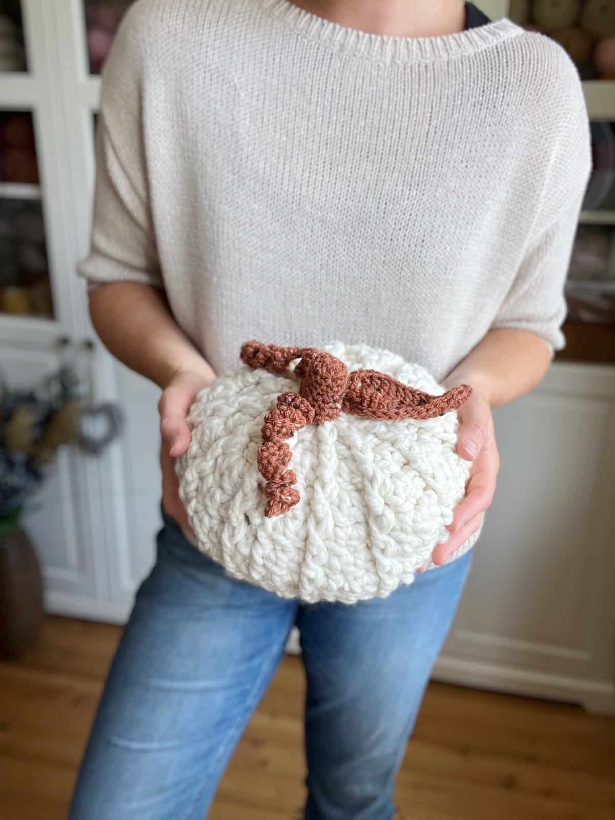 A woman holding a crocheted pumpkin.