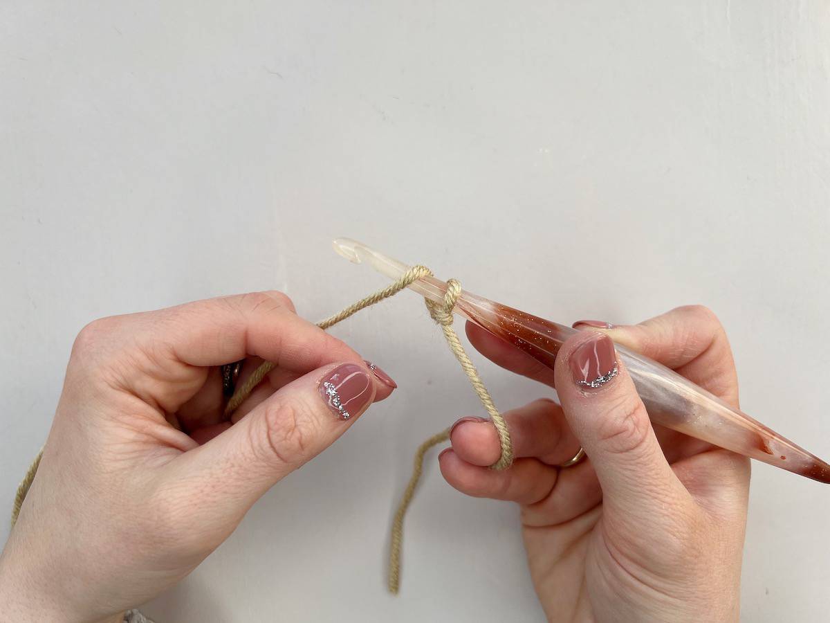 A person is creating a crochet chain stitch by wrapping the yarn around the hook.