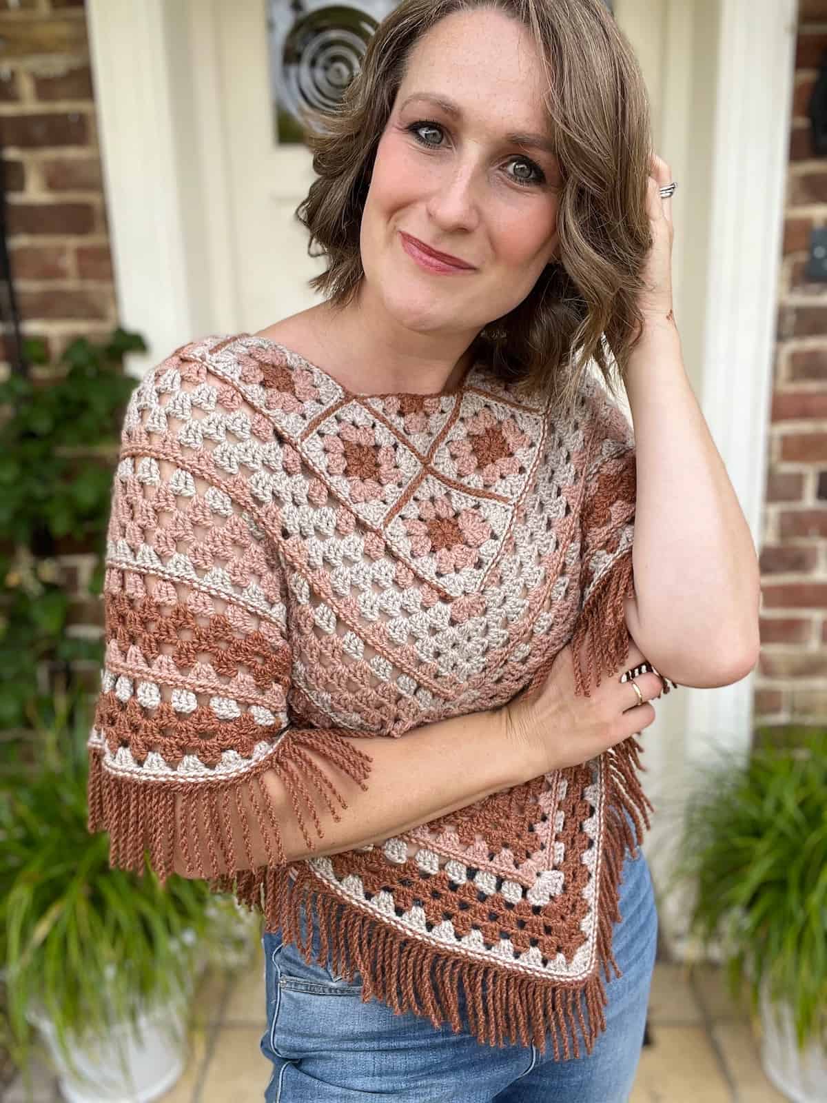 A woman wearing a crocheted poncho and jeans.