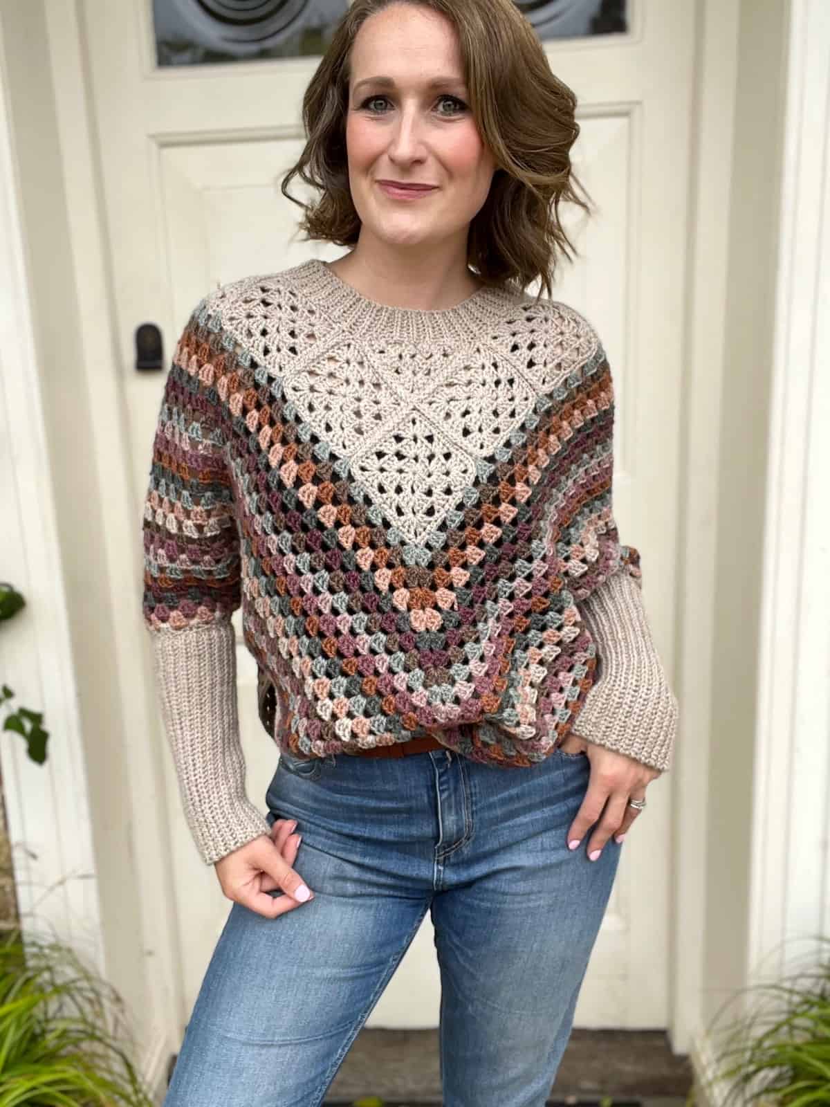 A woman wearing jeans and a sweater standing in front of a door.