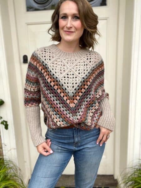 A woman wearing jeans and a sweater standing in front of a door.