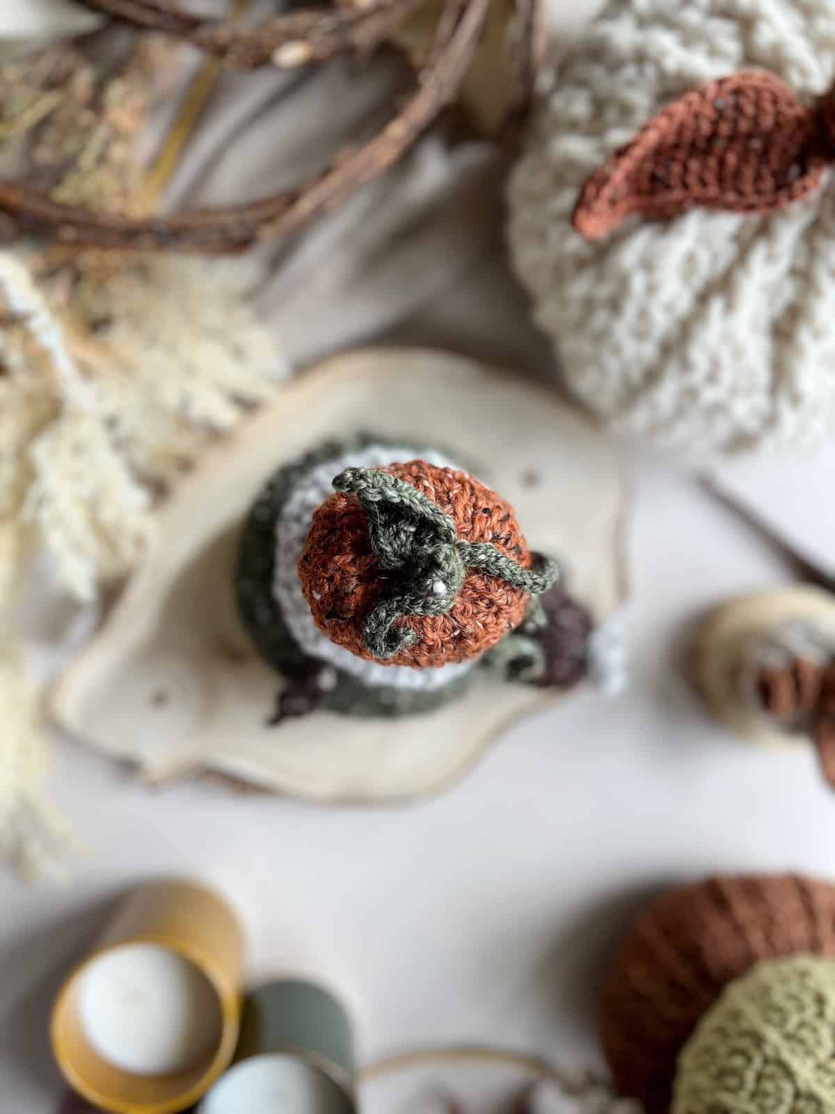A crochet pumpkin on a table next to a candle.